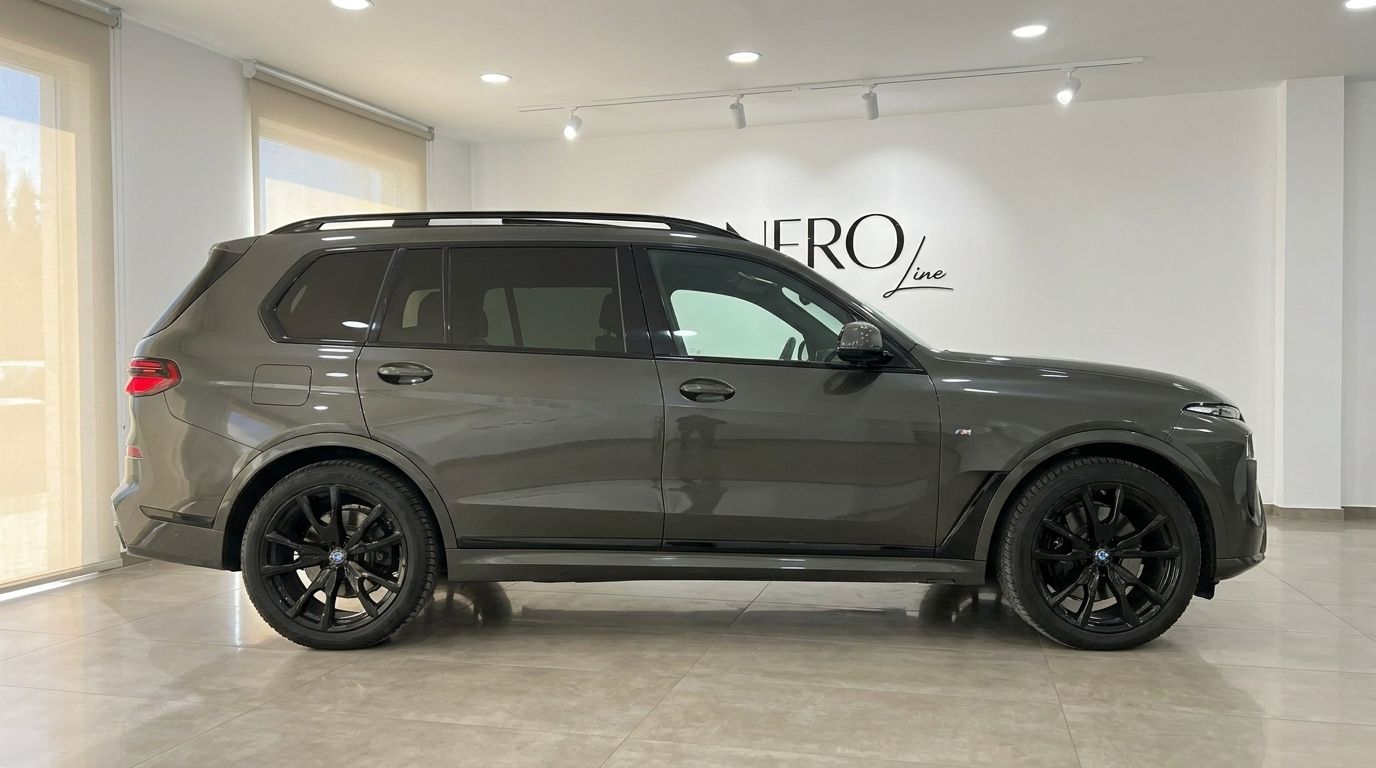 The luxurious 2025 BMW X7, in a sophisticated dark grey, is showcased from its elegant side profile in Alicante.
