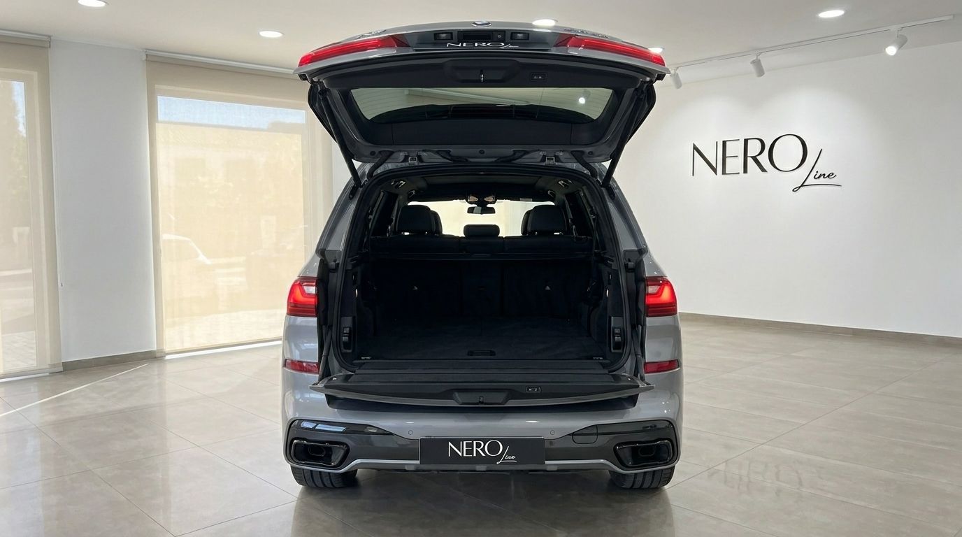 Rear view of a grey BMW X7 xDrive M Sport with its trunk open, revealing a spacious cargo area in a Marbella showroom.