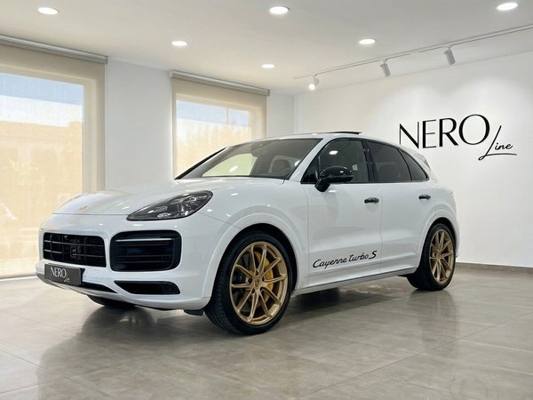 Porsche Cayenne Turbo S E-Hybrid — Showroom Alicante The white Porsche Cayenne Turbo S E-Hybrid with gold wheels is parked in a showroom in Alicante, shown from a front three-quarter view.