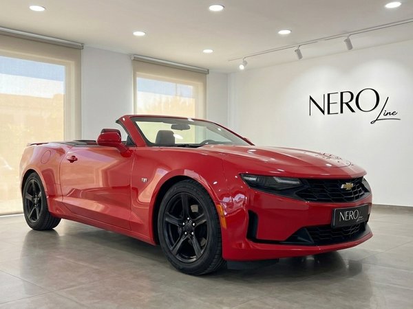 Chevrolet Camaro — Cabrio rosso ad Alicante Una Chevrolet Camaro cabriolet rosso brillante, con la capote abbassata, è parcheggiata in uno showroom ad Alicante.