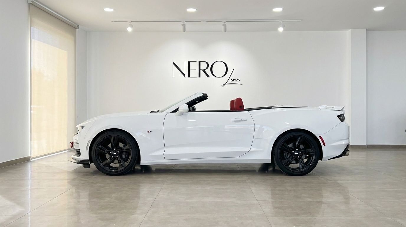 The white Chevrolet Camaro Cabrio 3.6, with its roof down and striking red interior, is showcased from a side profile in an Alicante showroom.