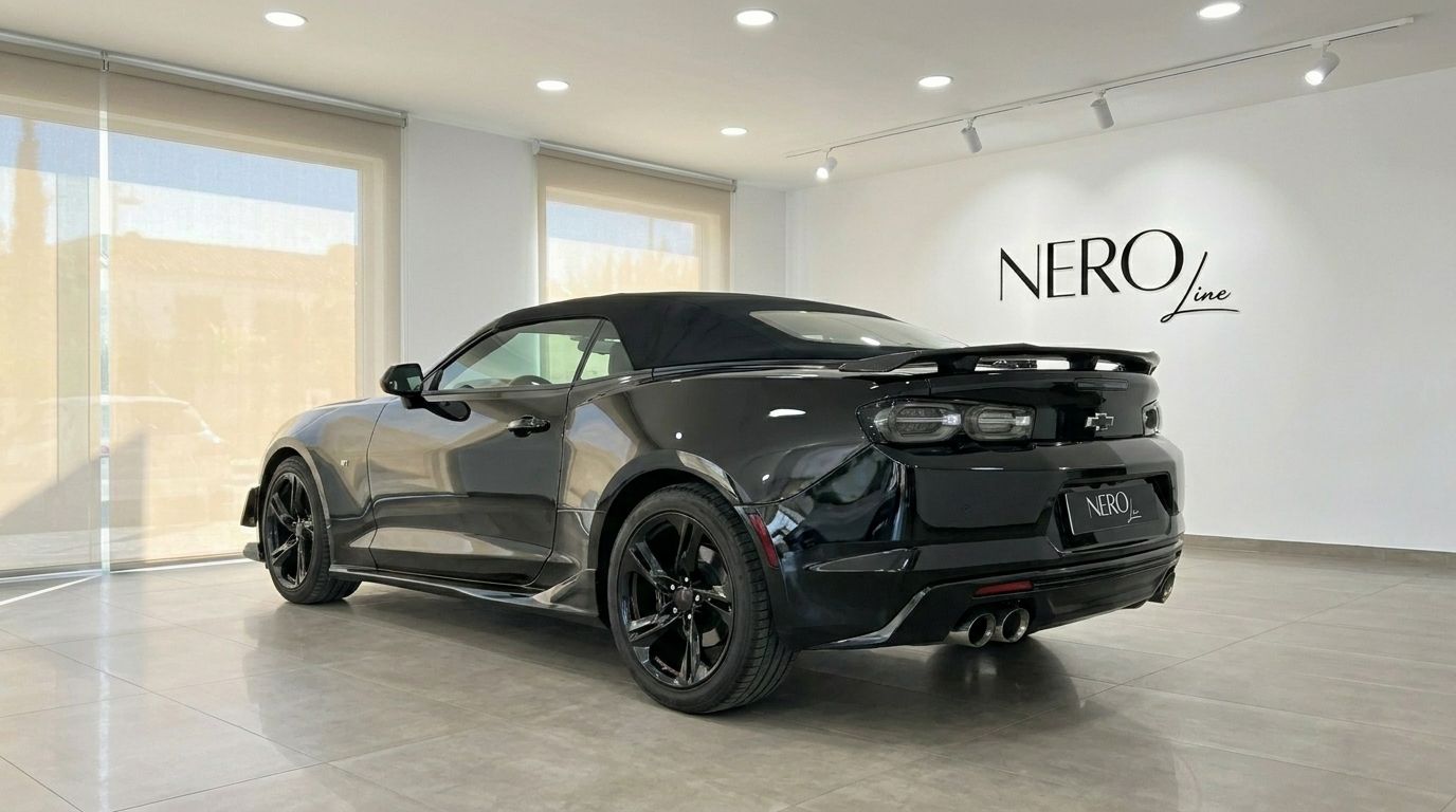 O Chevrolet Camaro Cabriolet preto de 2021, com a capota levantada, está estacionado no interior, exibindo a sua elegante vista traseira de três quartos em Alicante.
