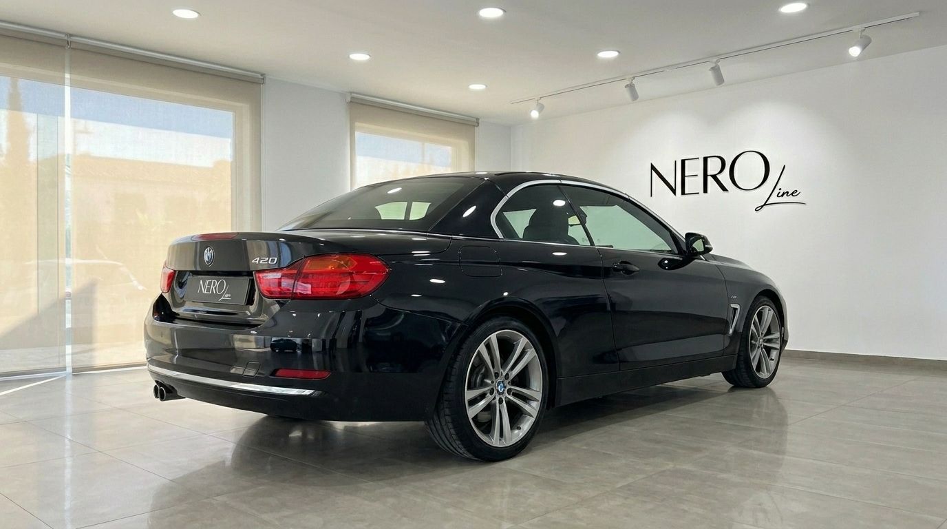 The black BMW 420 Cabriolet with its hardtop up, shown from a rear three-quarter angle in a bright Alicante showroom.