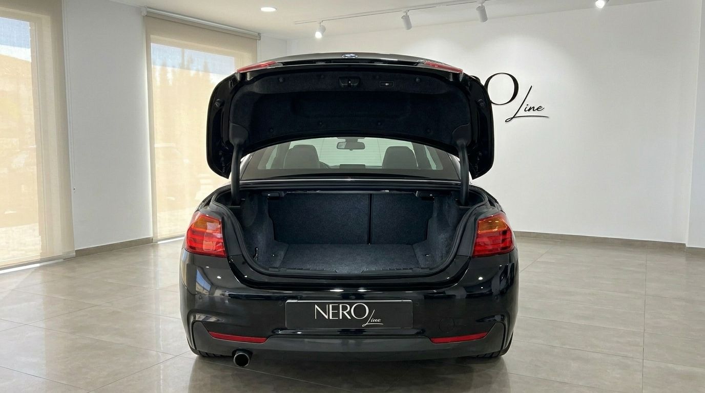 The black BMW 420 Cabriolet is shown from the rear with its trunk open, revealing the spacious cargo area in Alicante.