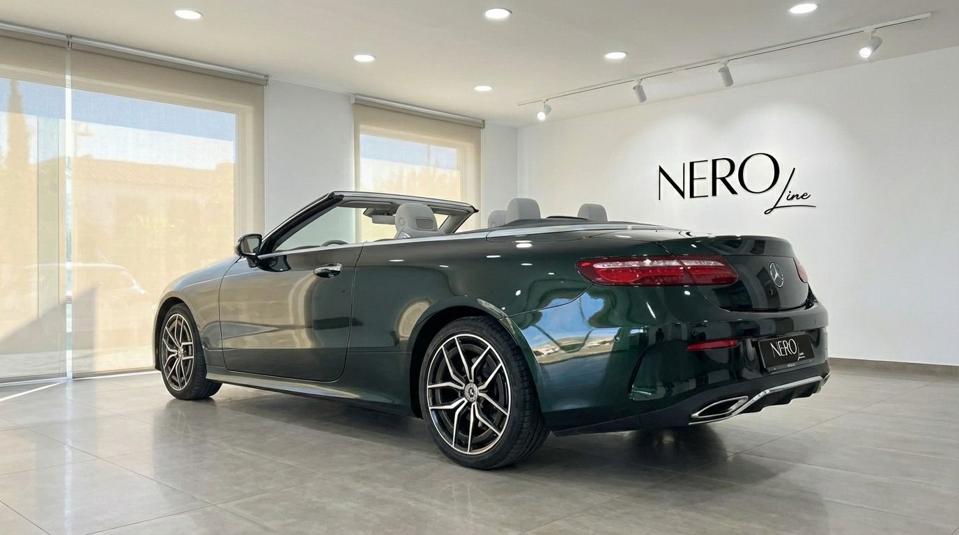 A dark green Mercedes-Benz E300 Cabrio with its top down and light grey interior, displayed in a showroom in Alicante.