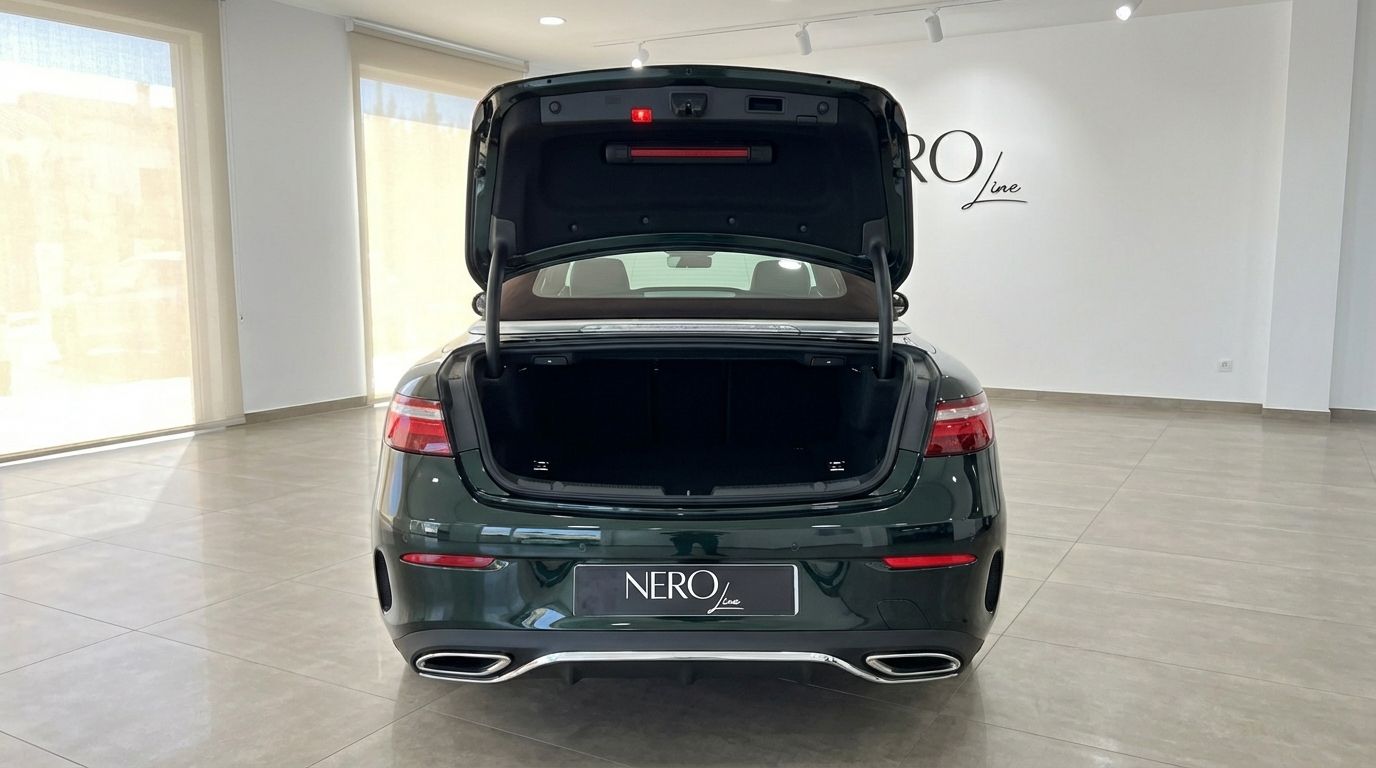 The dark green Mercedes-Benz E300 Cabrio is shown from the rear with its trunk open in a showroom in Alicante.