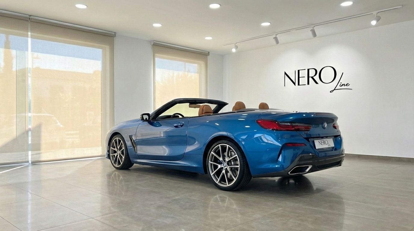 The sky blue BMW M850i Carbon Core Edition convertible, with its brown leather interior and top down, is showcased from a rear-three-quarter angle in a bright Alicante showroom.