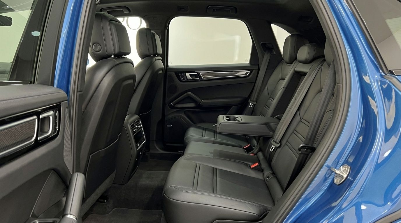 The luxurious black leather rear seats and door panel of the blue Porsche Cayenne in Mallorca, featuring a central armrest.