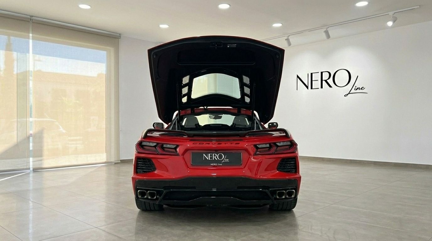 Red Chevrolet Corvette Stingray C8 from the rear, with its engine cover open, displayed in a modern showroom.