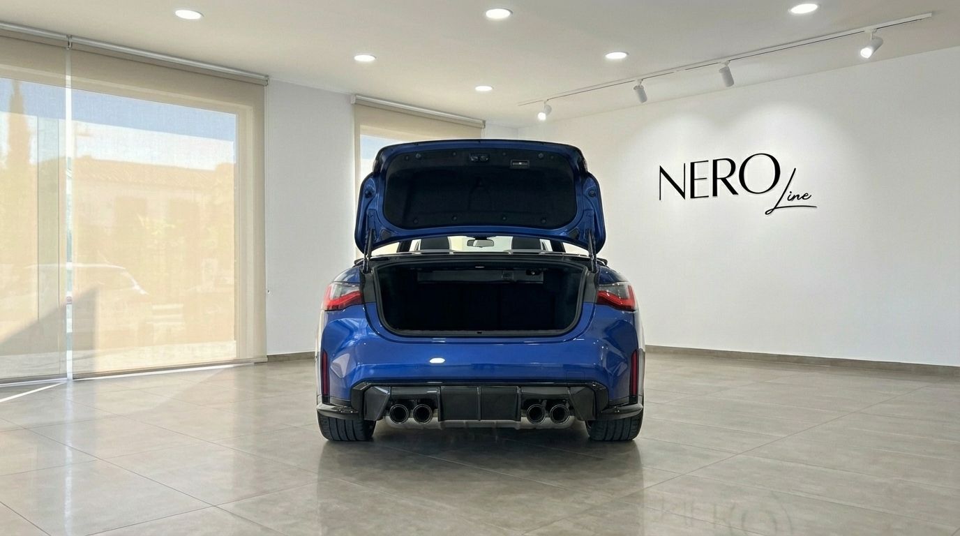 The metallic blue 2025 BMW M4 Competition Convertible is shown from the rear with its trunk open in a Barcelona showroom.