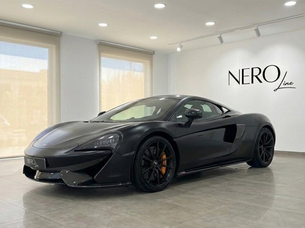 McLaren 570S — Supercar Noir Mat à Marbella La supercar McLaren 570S noir mat est présentée de trois quarts avant dans un showroom lumineux à Marbella.