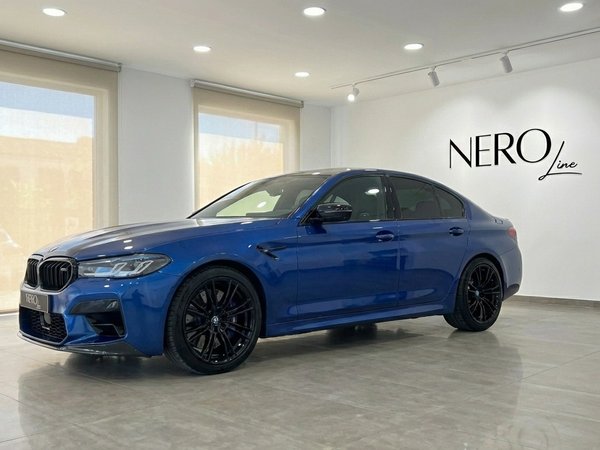 BMW M5 Competition Hybrid — Front-side showroom view A metallic dark blue BMW M5 Competition Hybrid luxury sedan parked in a showroom in Marbella, viewed from the front-side.