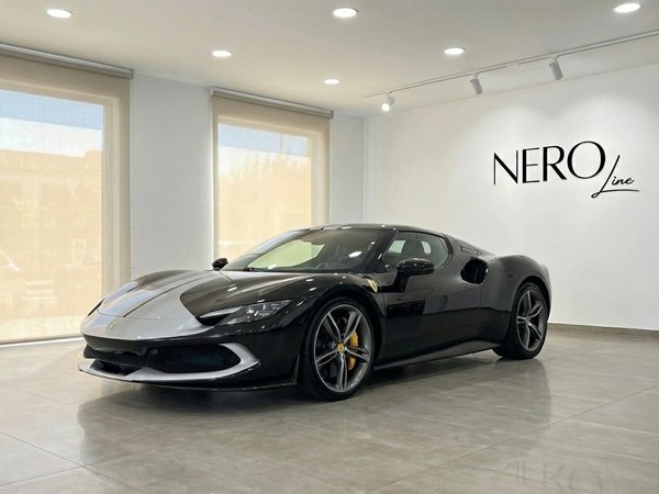 Ferrari 296 GTB — Vista frontal tres cuartos, Madrid Un Ferrari 296 GTB negro y plateado de 2024 se exhibe en un moderno salón de exposición en Madrid, visto desde un ángulo frontal tres cuartos.