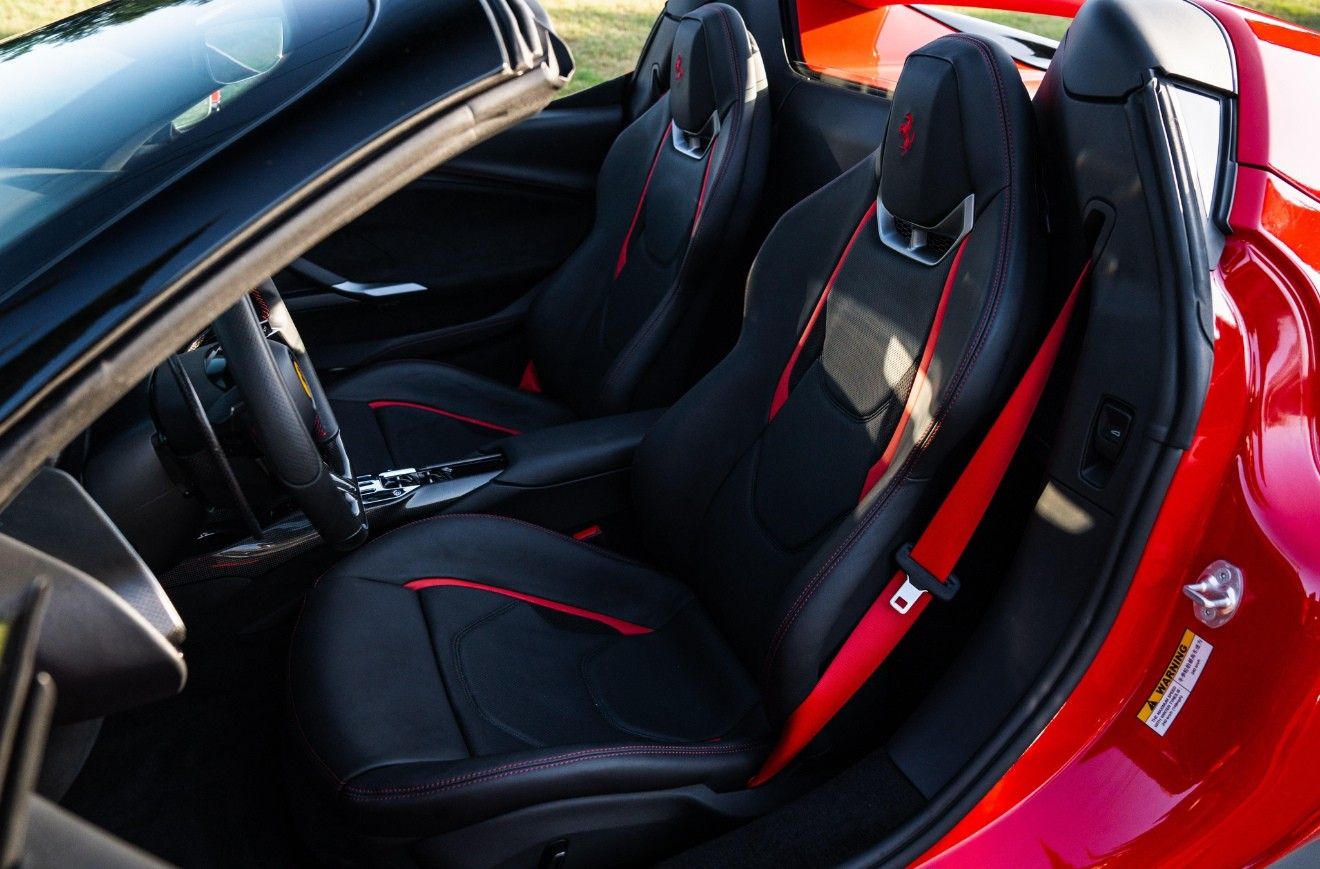 Interior del Ferrari 296 GTS mostrando lujosos asientos de cuero negro con costuras y cinturones de seguridad rojos a juego en Madrid.