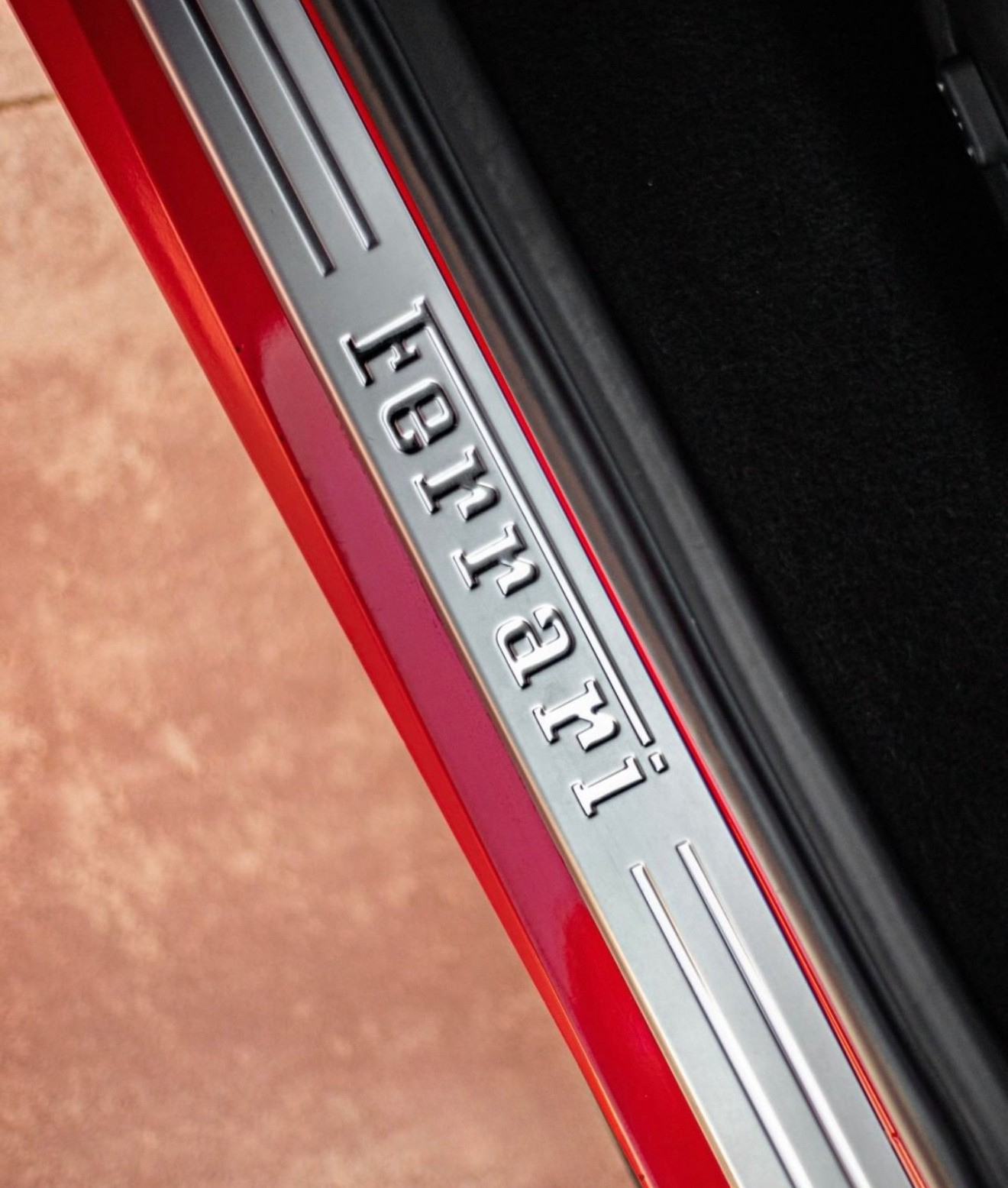 A close-up of the Ferrari 488 Spider's metallic door sill plate with the Ferrari logo, set against the racing red exterior and black interior in Alicante.