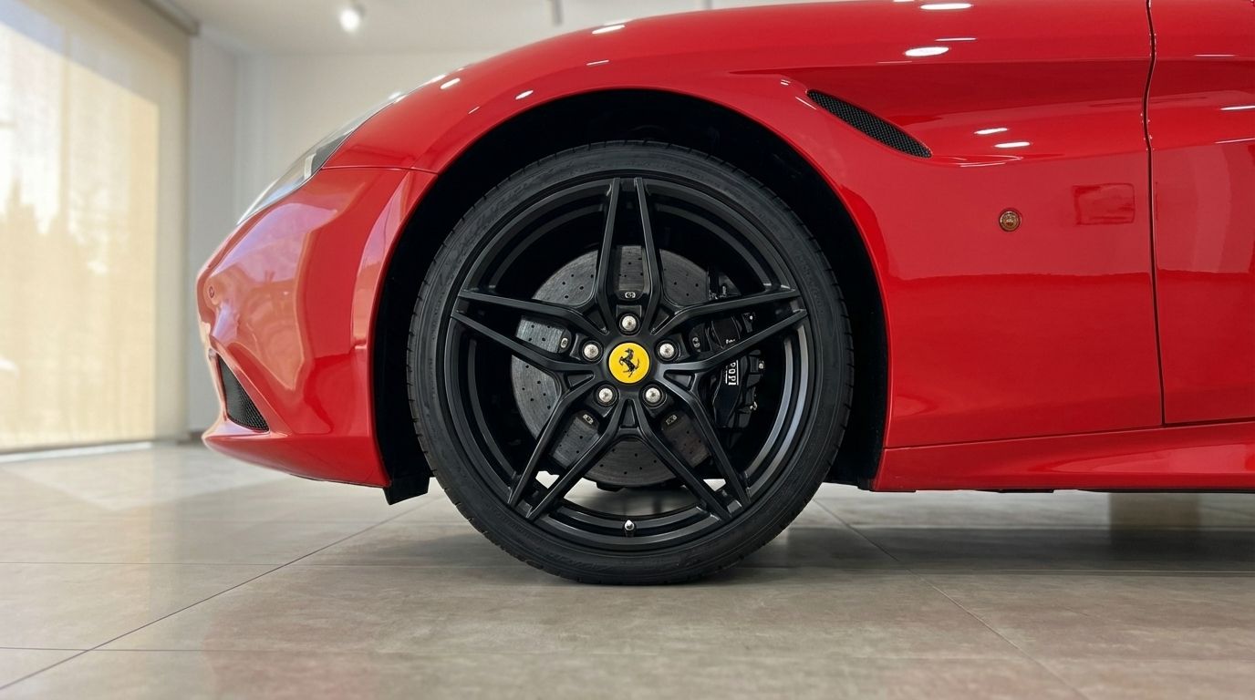 A close-up of the red Ferrari California's front wheel and fender, showcasing its black multi-spoke rim and brake system in Alicante.
