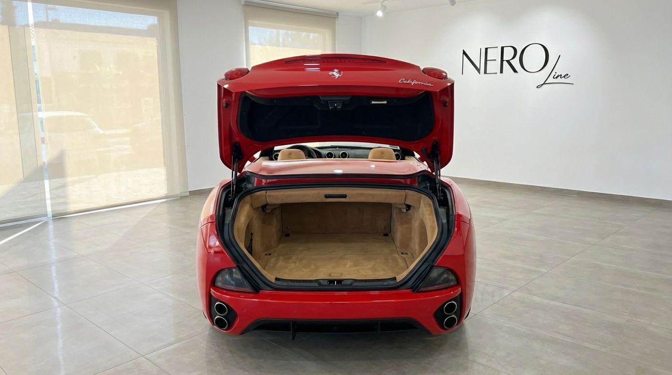 The red Ferrari California is shown from the rear with its trunk open, revealing the beige interior and convertible top compartment in Alicante.