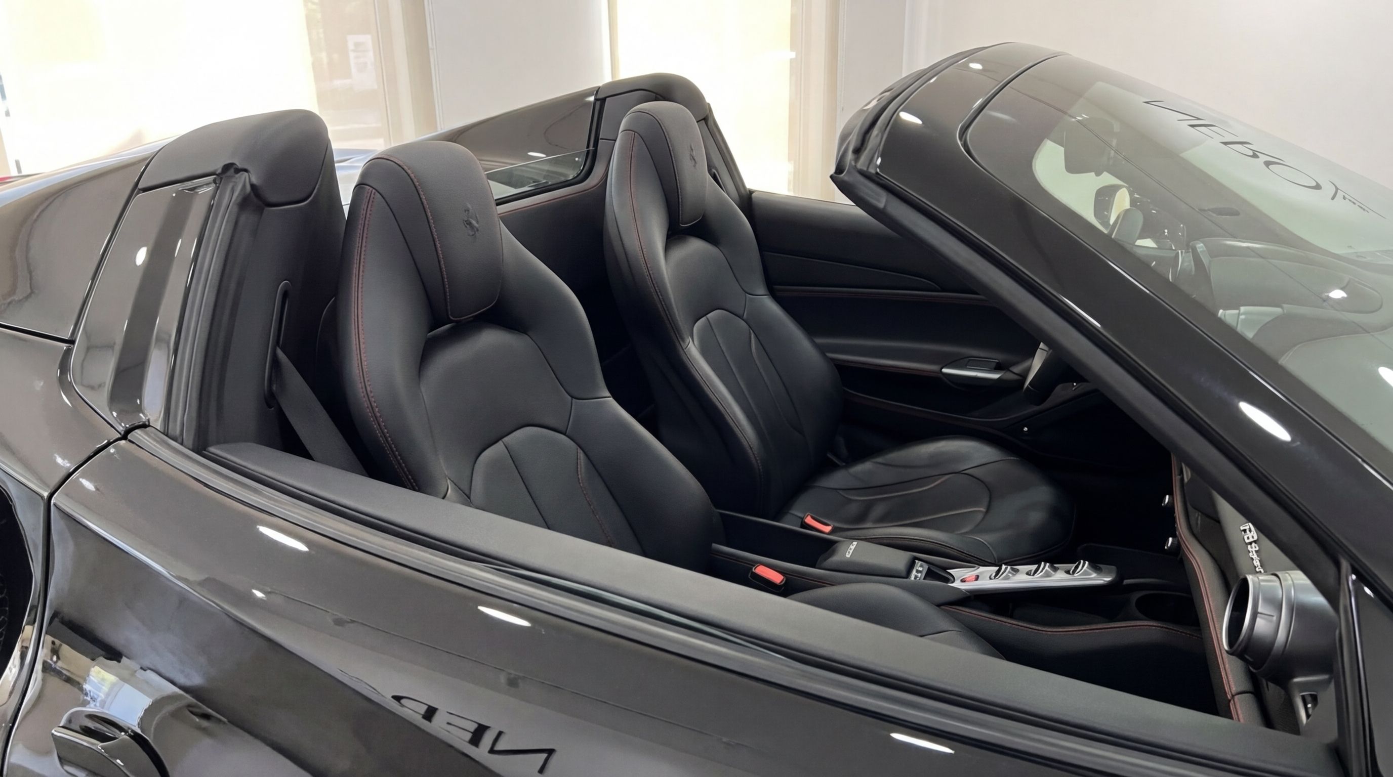 The luxurious black leather interior of the Ferrari F8 Spider with red stitching, seen from the side with the top down in Ibiza.