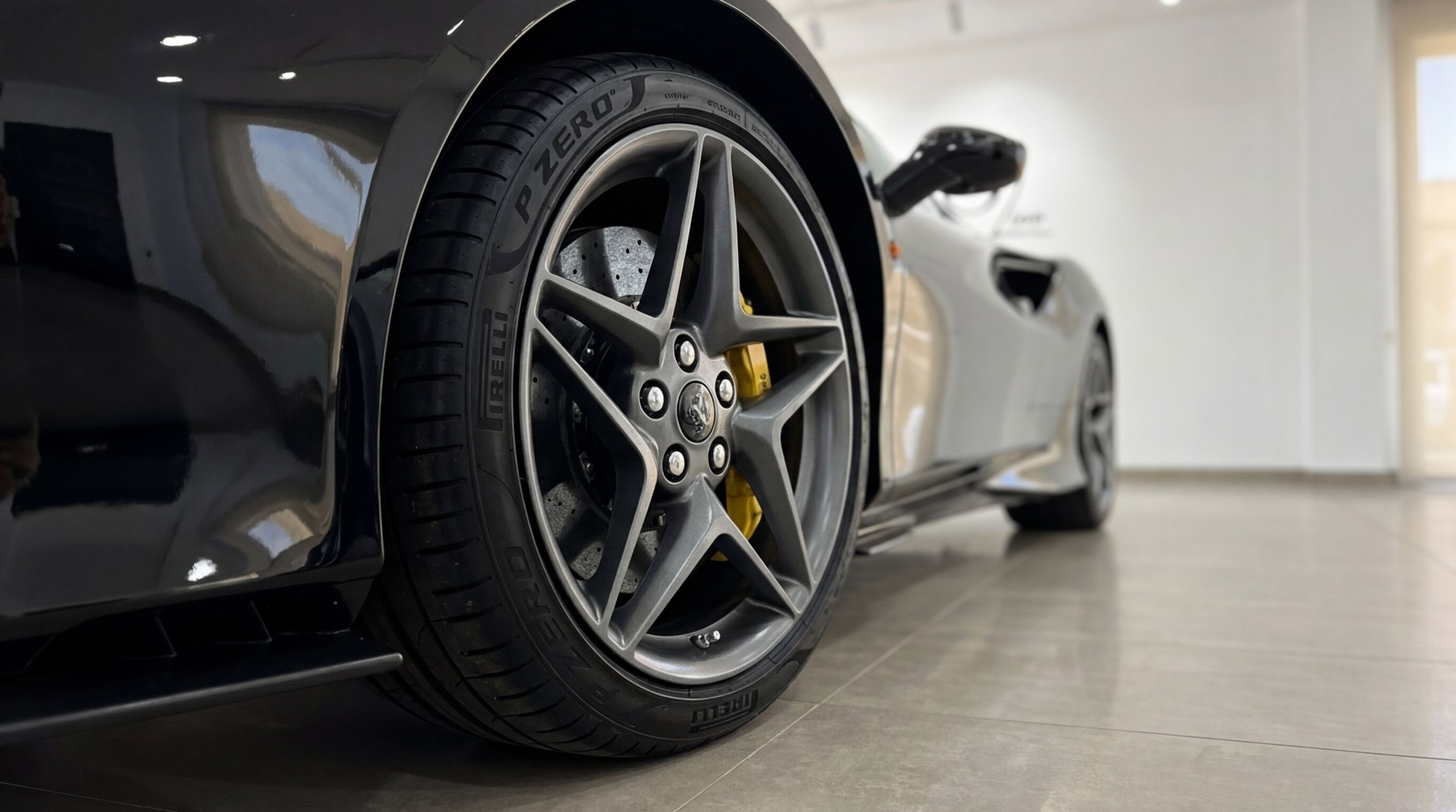 Close-up of the black Ferrari F8 Spider's rear wheel, featuring a grey multi-spoke rim, yellow brake caliper, and Pirelli P Zero tire in Ibiza.