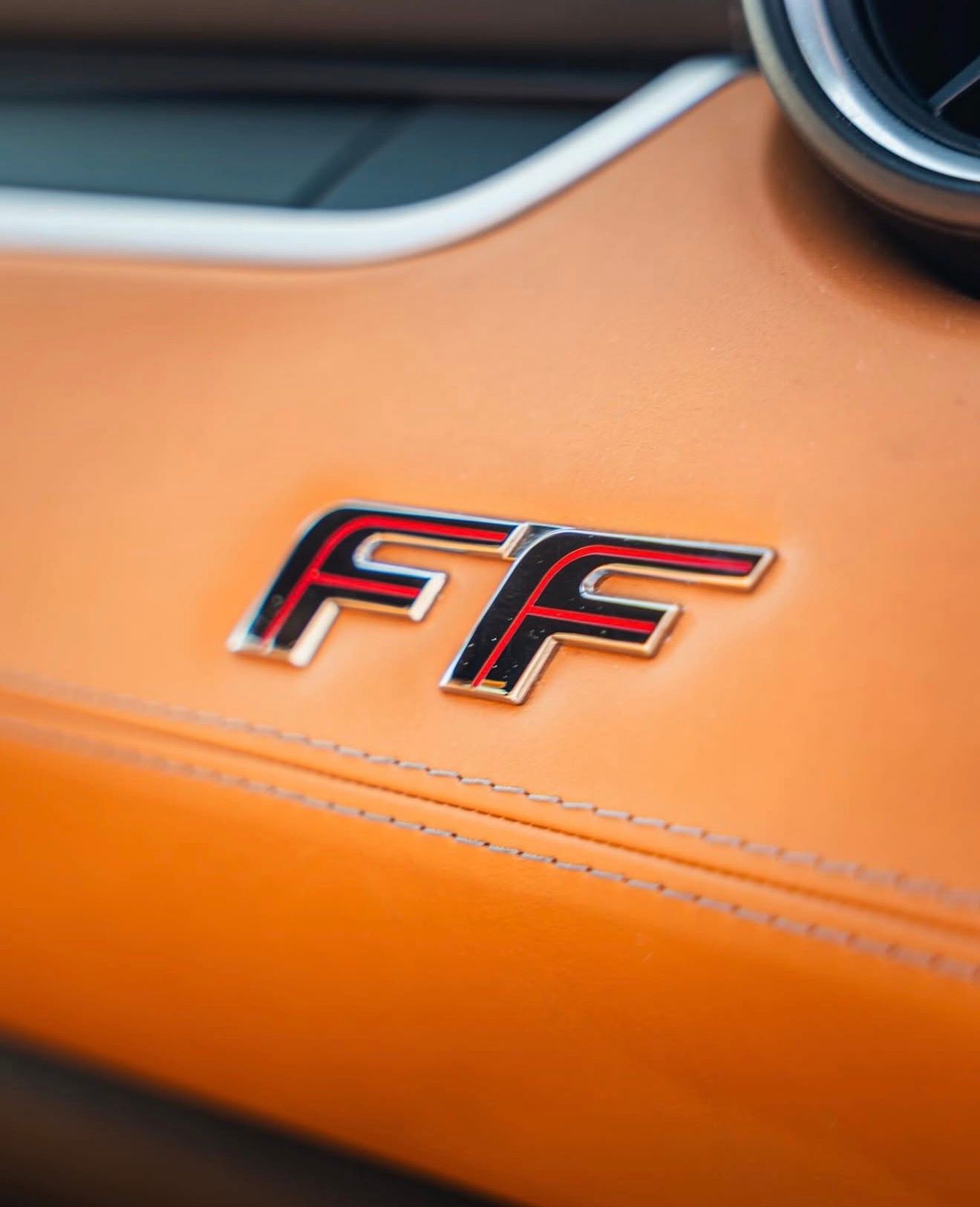 Close-up of the Ferrari FF's 'FF' emblem on a tan leather interior panel with visible stitching, highlighting luxury details in Valencia.