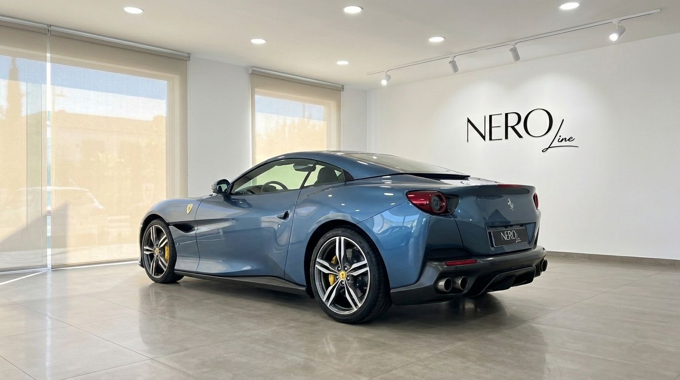 The metallic Blu Roma 2022 Ferrari Portofino M is showcased from a rear three-quarter angle in a bright showroom in Mallorca.