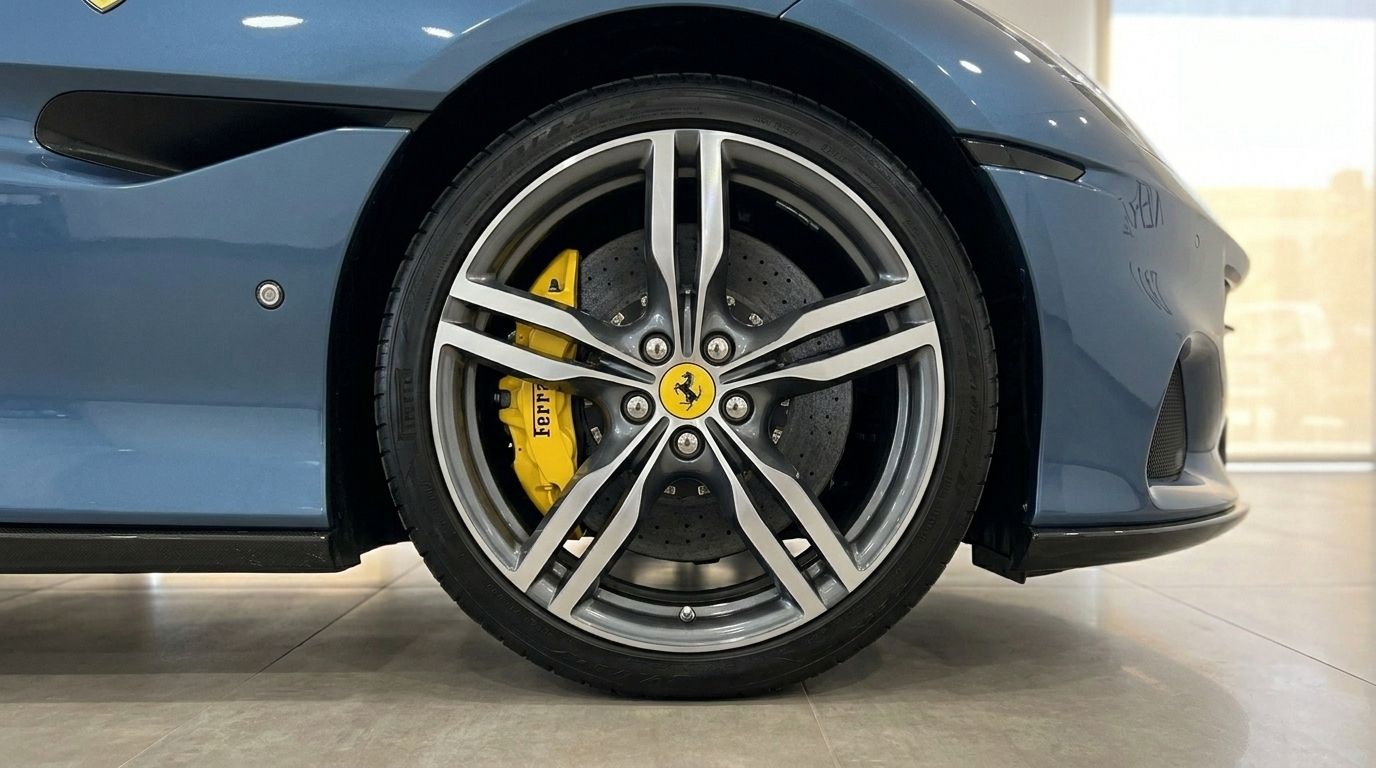 The front wheel of a metallic Blu Roma Ferrari Portofino M, showcasing its multi-spoke alloy rim and yellow brake caliper in Mallorca.