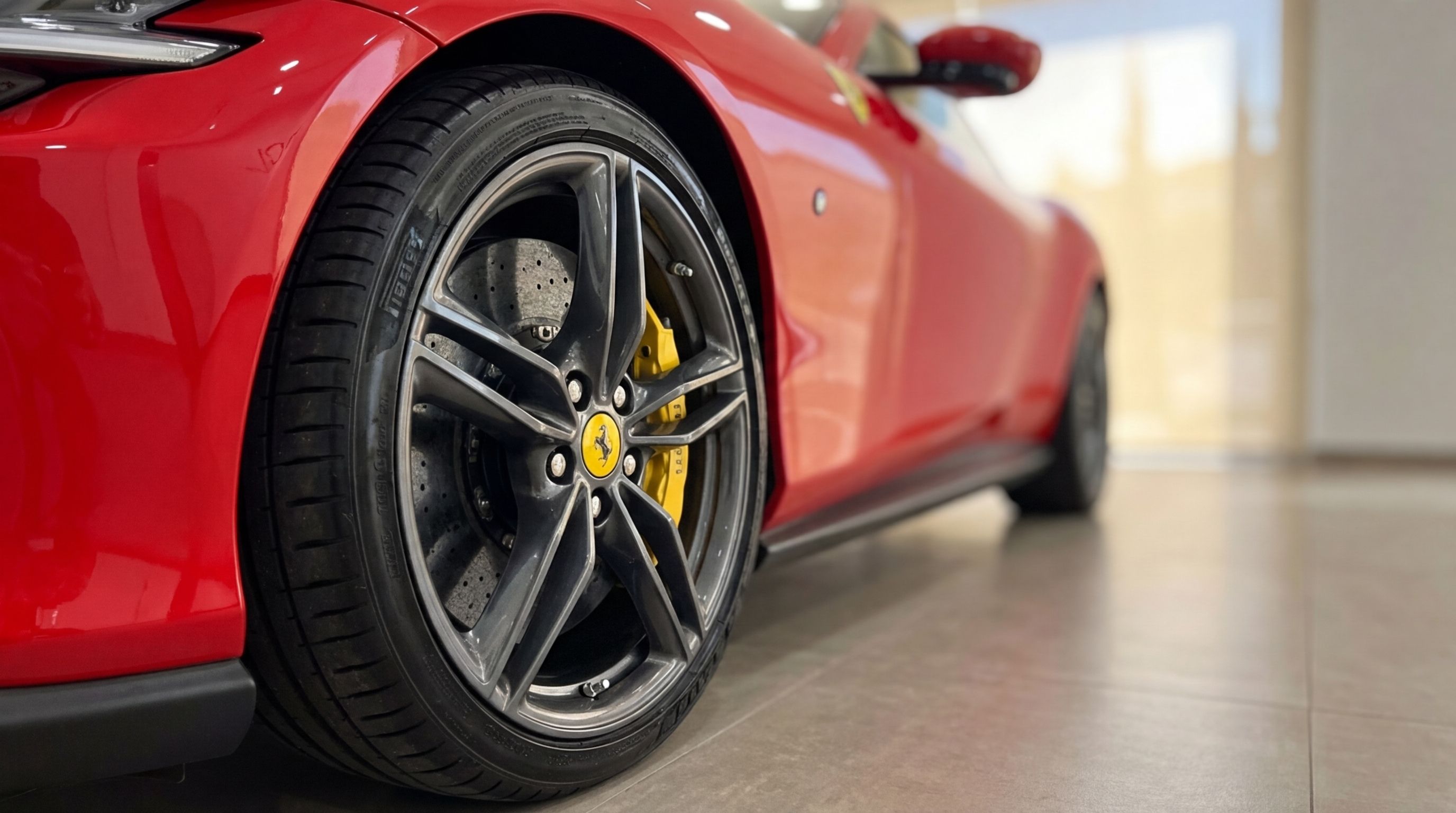 A close-up view of the racing red Ferrari Roma's front wheel, showcasing the dark alloy rim and bright yellow brake caliper in Barcelona.