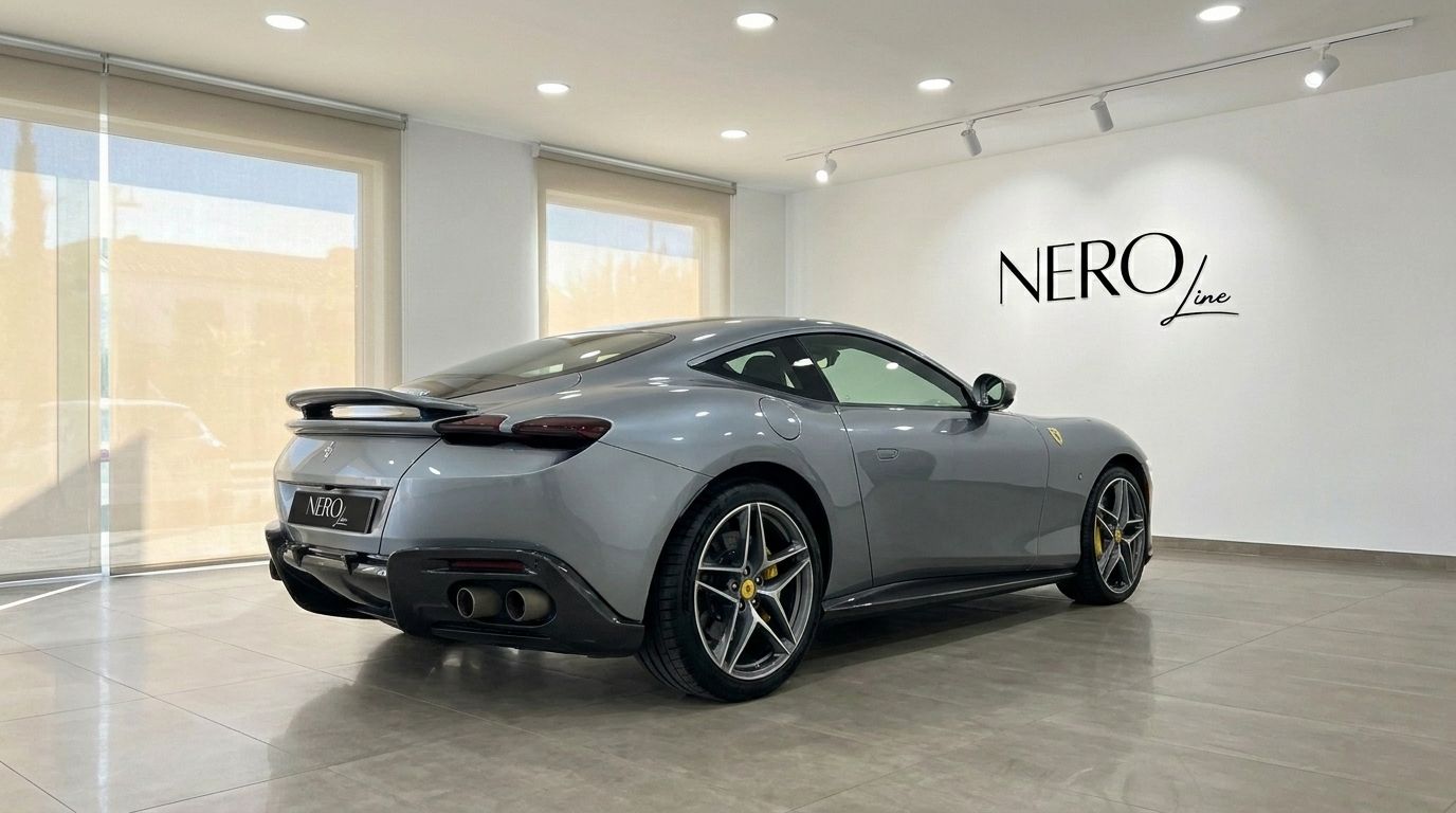 El elegante Ferrari Roma gris de 2022 se exhibe desde una vista trasera tres cuartos en un moderno showroom de Madrid, con el logo de Nero Line.