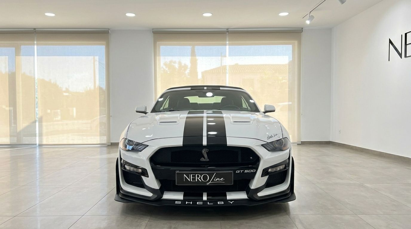 A white Ford Mustang 2.3 EcoBoost Convertible with black racing stripes is parked front-on in a showroom in Benidorm.