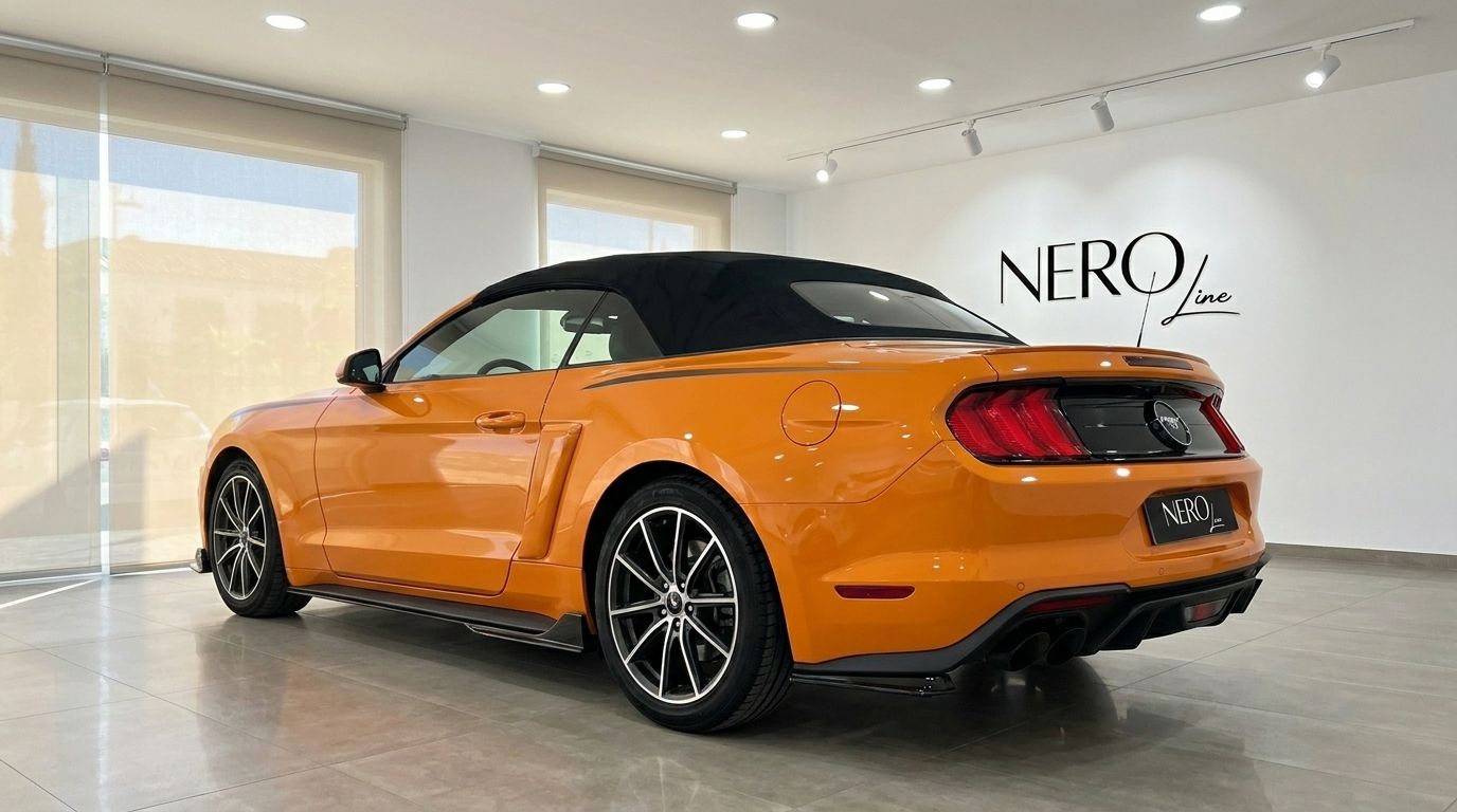 An orange Ford Mustang 2.3 EcoBoost Convertible is shown from a rear three-quarter view with its black soft top up, indoors in Alicante.