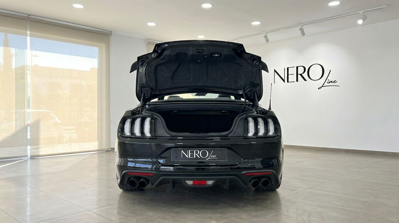 The black Ford Mustang GT 5.0 is shown from the rear with its trunk open, parked inside a modern showroom in Alicante.