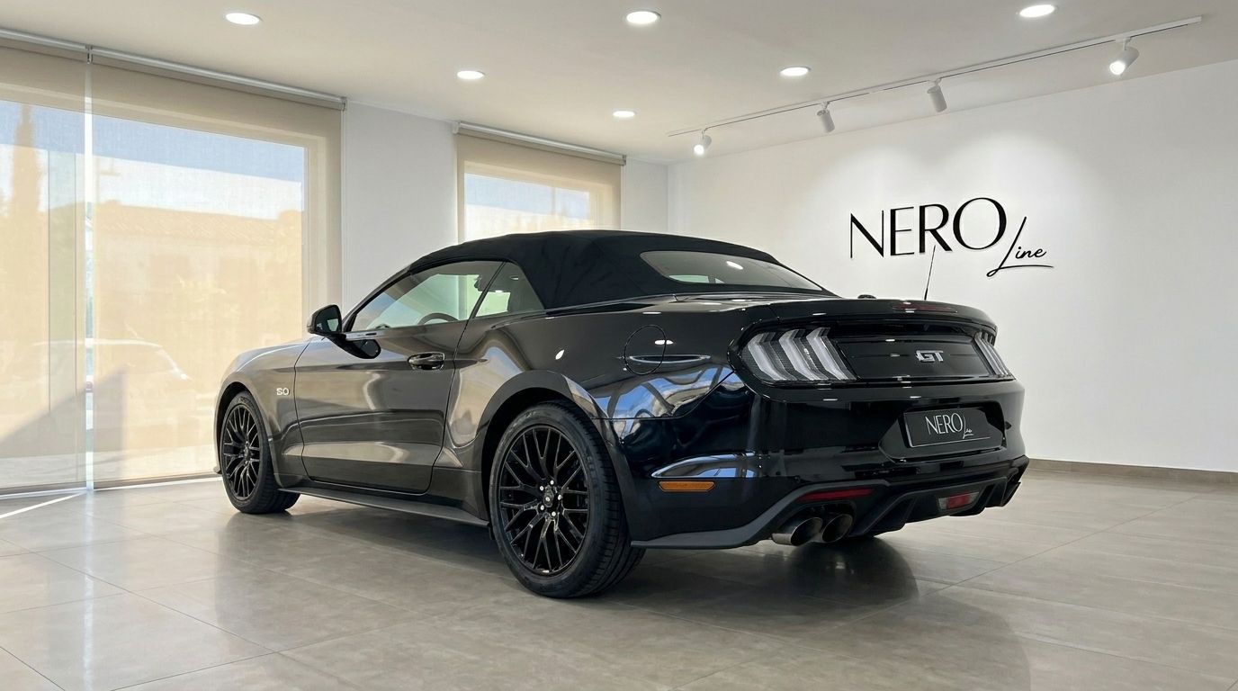 The black 2023 Ford Mustang GT 5.0 convertible is showcased from a rear three-quarter view in a bright showroom in Alicante.
