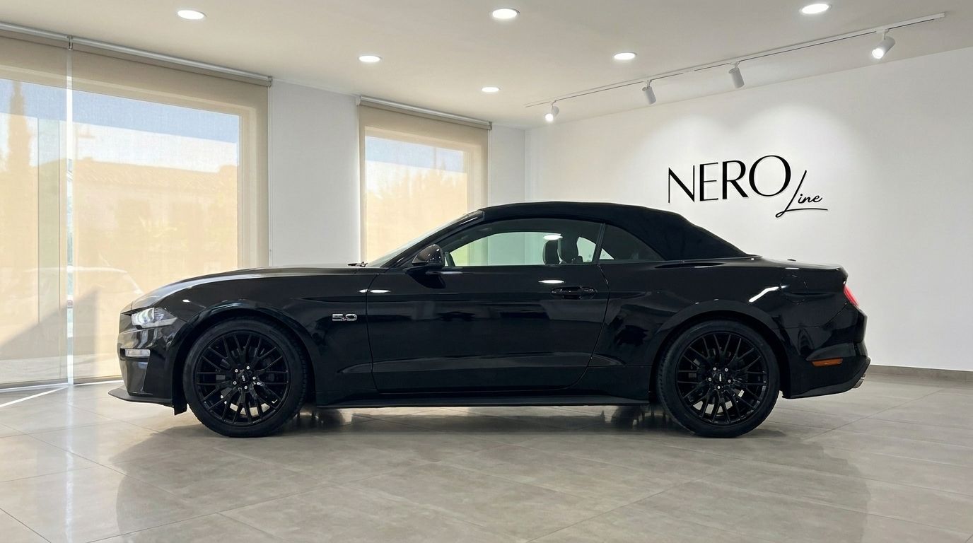 A black 2023 Ford Mustang GT 5.0 convertible is parked in a showroom, viewed from its side profile in Alicante.