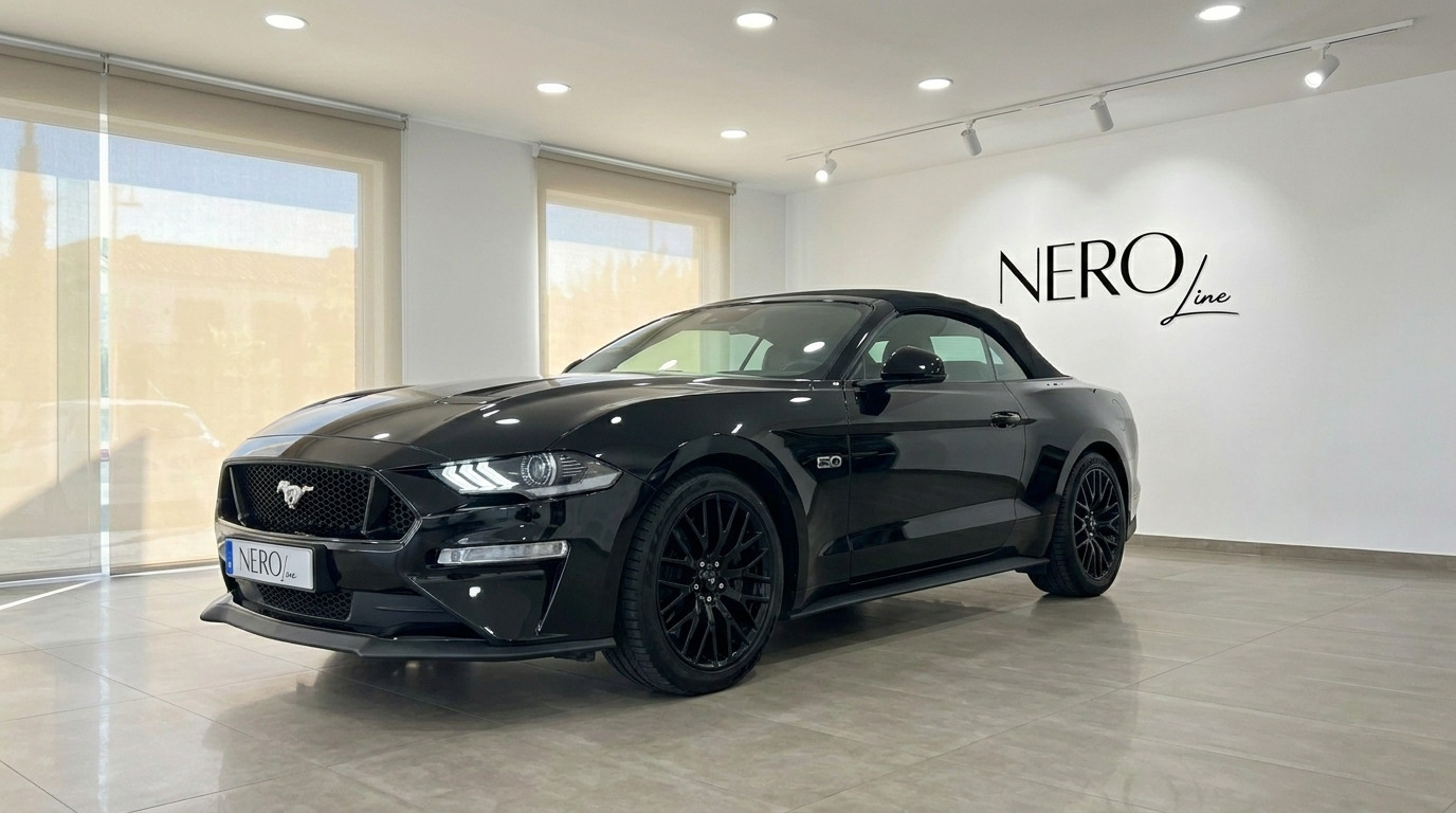 Ford Mustang GT 5.0 — Black Convertible, Alicante A sleek black Ford Mustang GT 5.0 convertible is displayed from a front three-quarter view in a bright Alicante showroom.