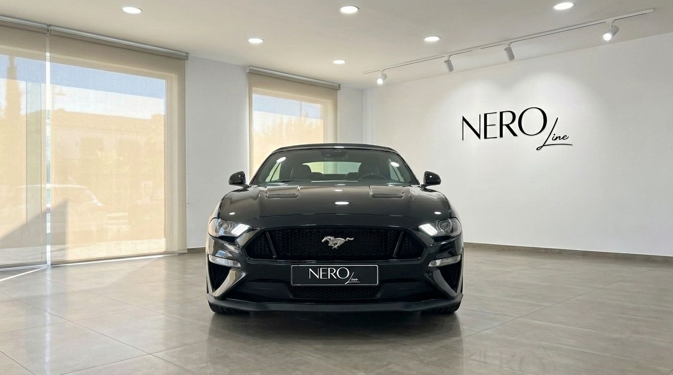 The black Ford Mustang GT 5.0 is prominently displayed from the front, parked indoors in Alicante, showcasing its aggressive grille and headlights.