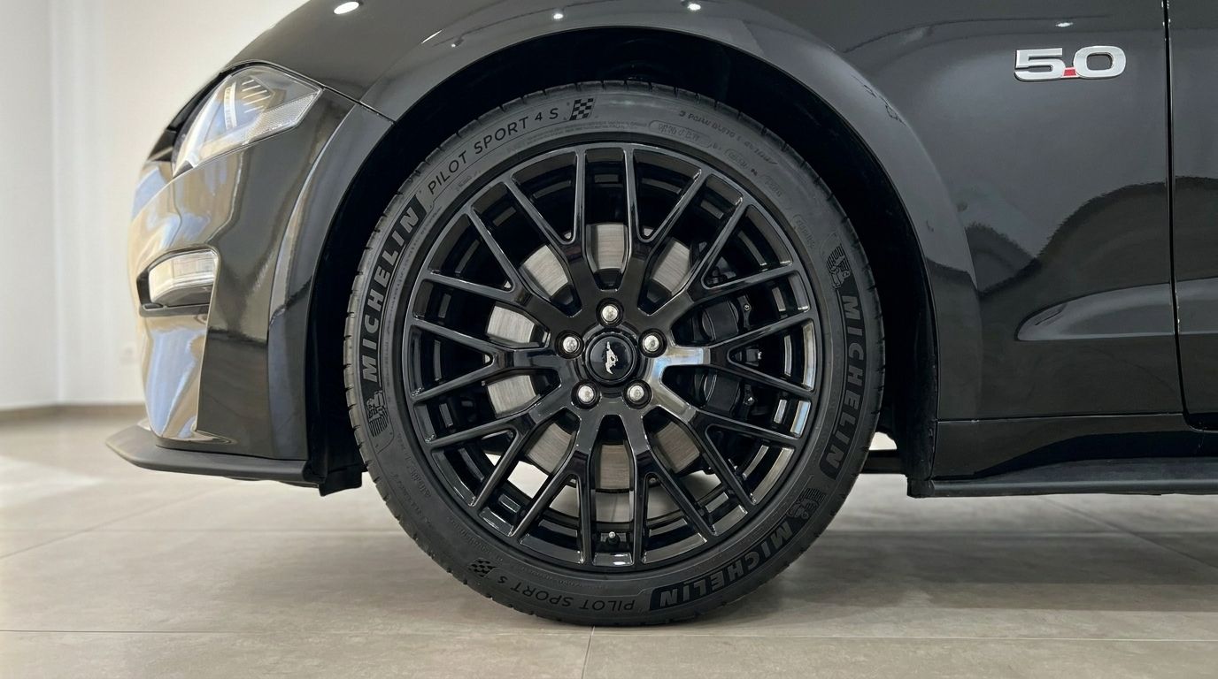A close-up of the black Ford Mustang GT 5.0's front wheel with a multi-spoke rim and Michelin tire, showing the fender and '5.0' badge in Alicante.