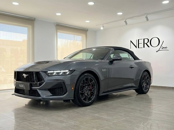 Ford Mustang GT Cabrio (2025) — Vista showroom La Ford Mustang GT Cabrio (2025) grigio carbonizzato metallizzato è esposta da un'angolazione anteriore a tre quarti in uno showroom a Madrid.