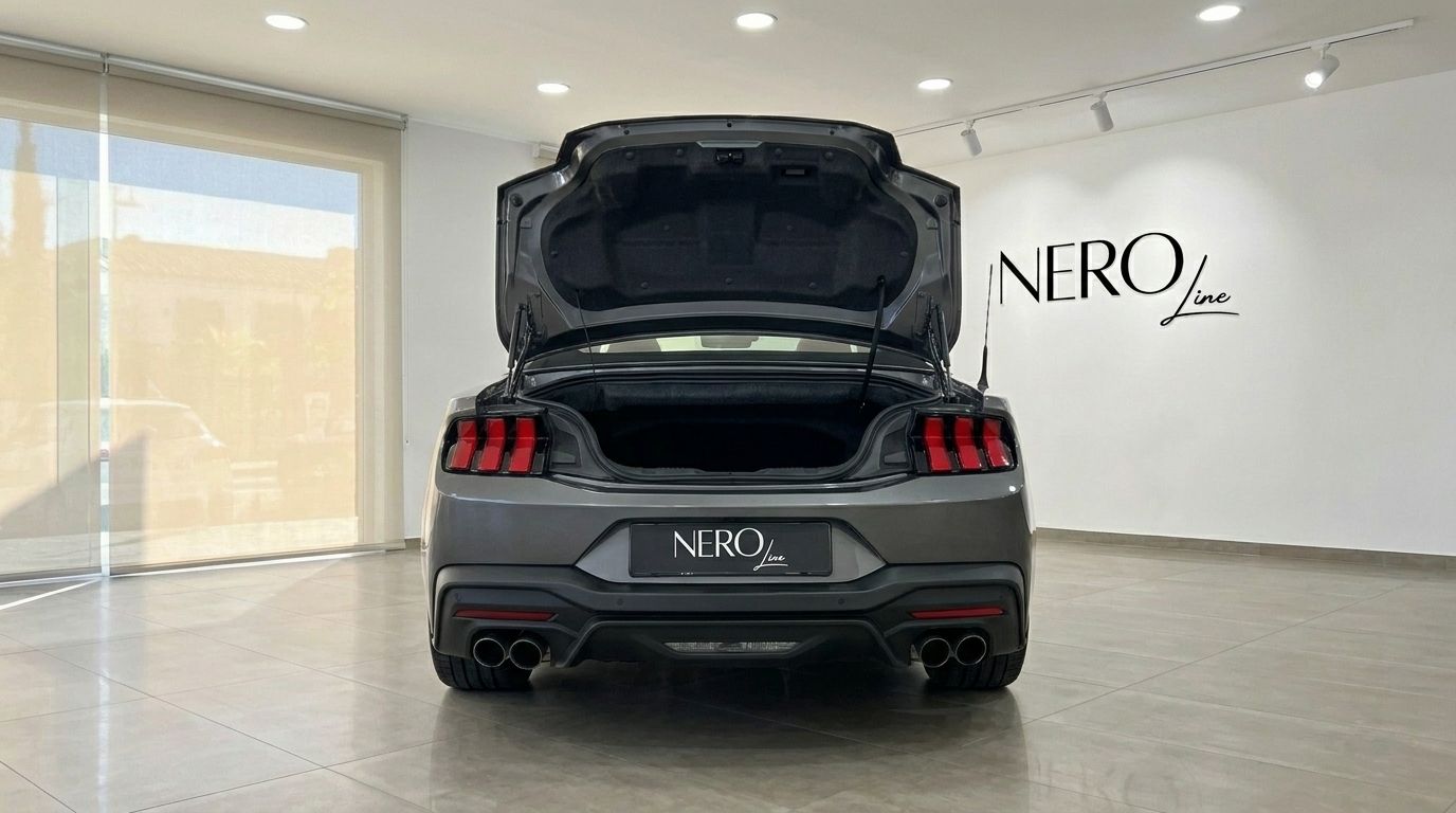 La Ford Mustang GT Cabrio (2025) grigio carbonizzato metallizzato è mostrata da dietro con il bagagliaio aperto in uno showroom di Madrid.