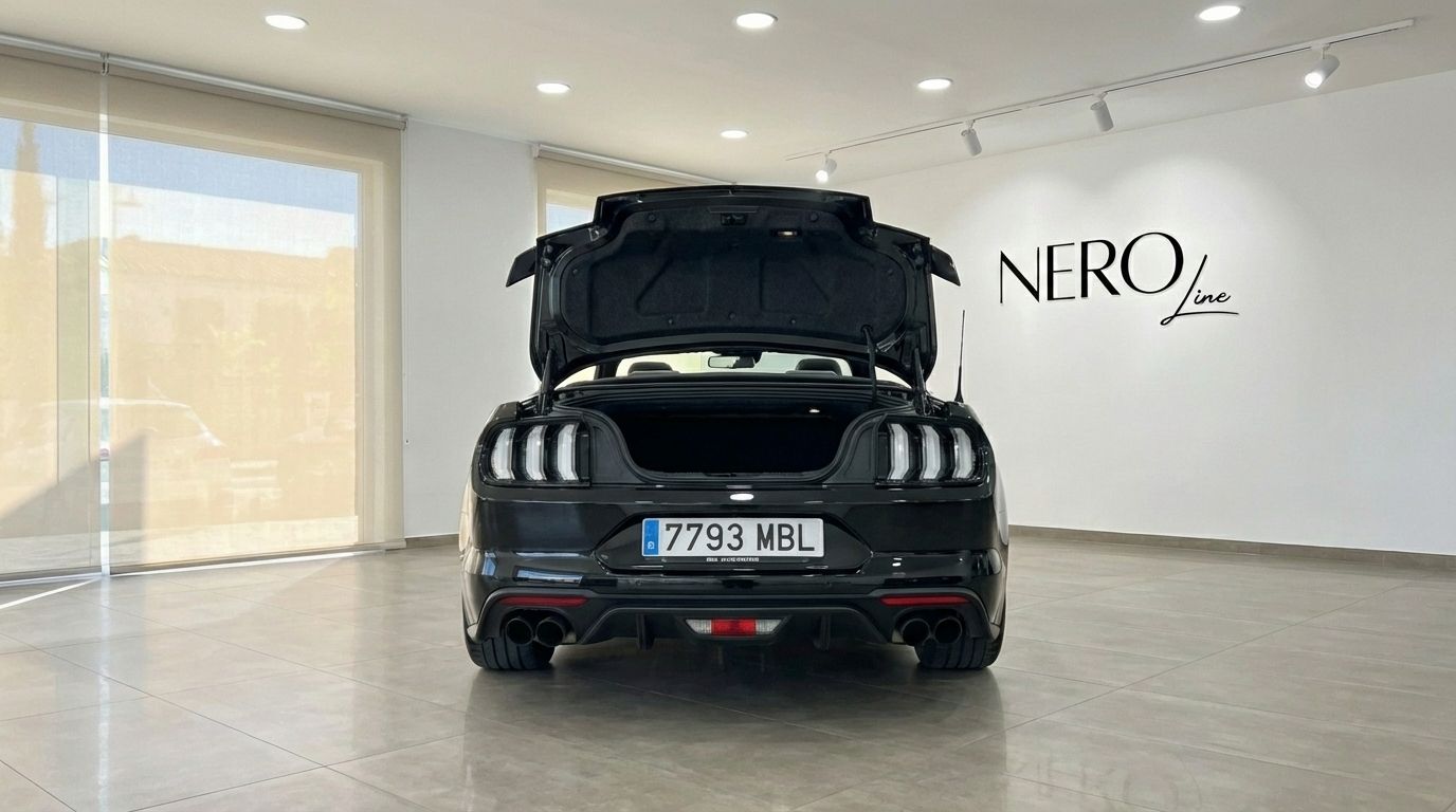 Rear view of a black Ford Mustang GT Convertible with its trunk open, parked in a showroom in Barcelona.