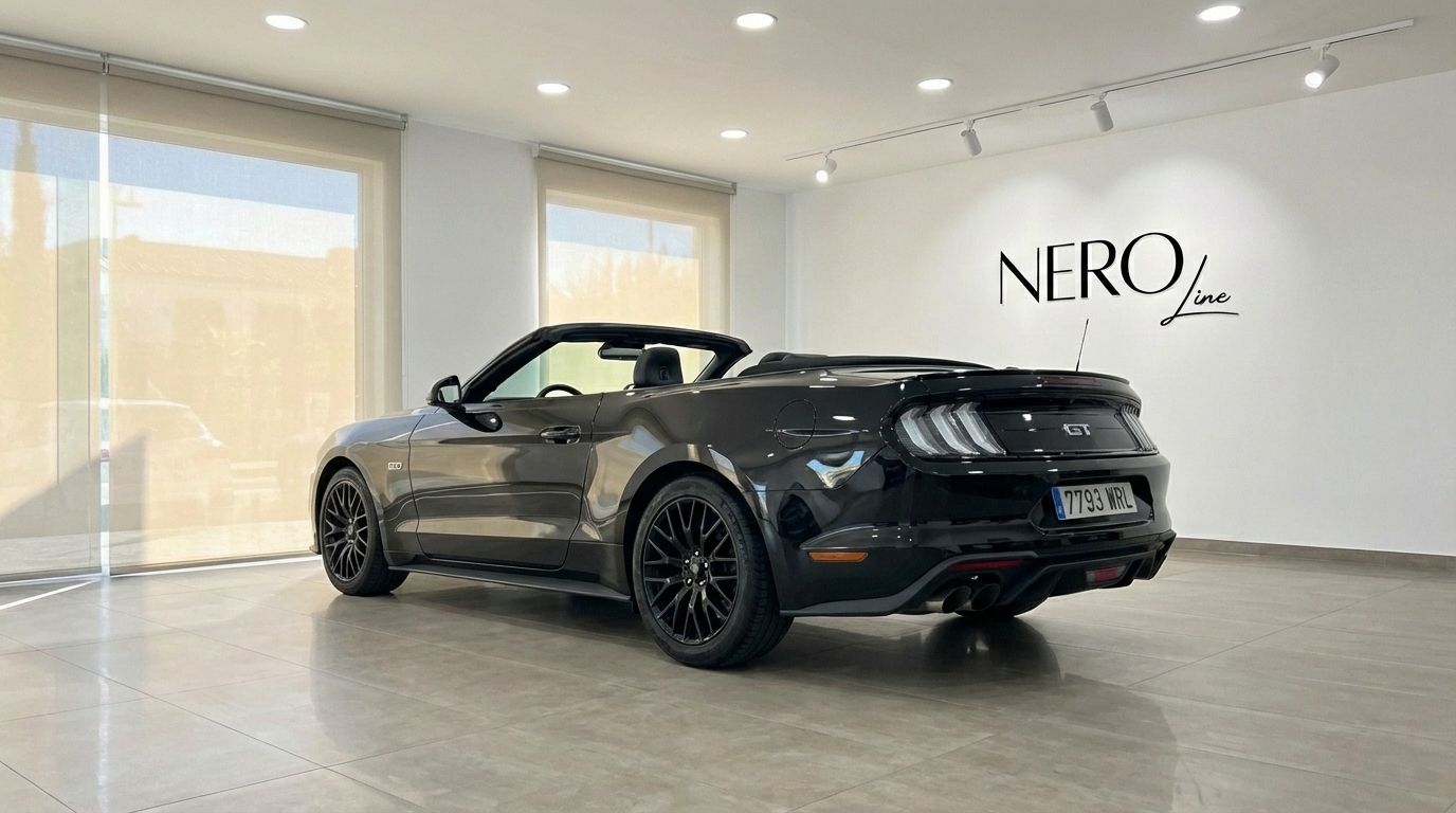 The black Ford Mustang GT Convertible is showcased from a rear three-quarter angle with its top down, parked in a modern showroom in Barcelona.