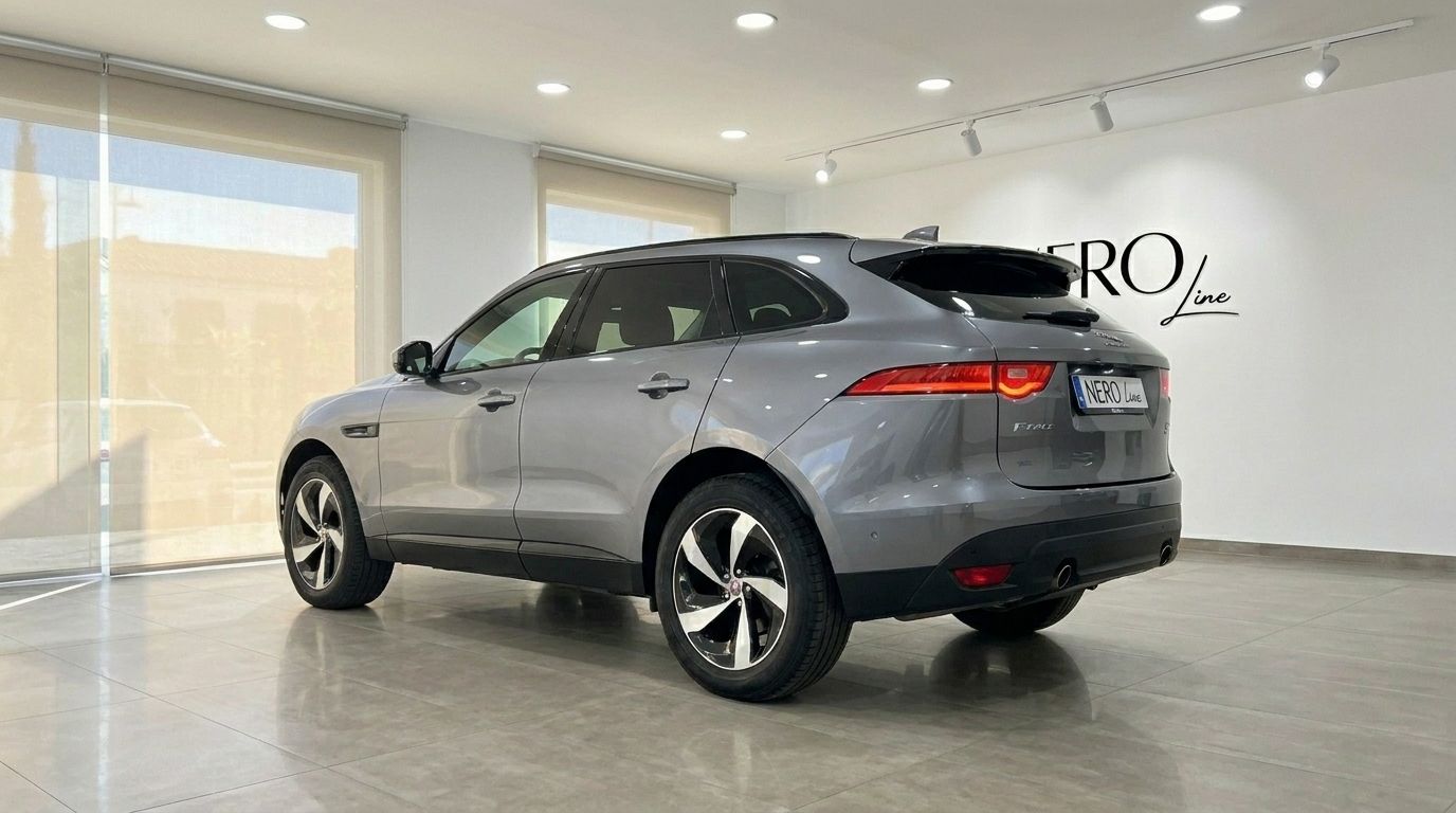 A sleek grey 2022 Jaguar F-Pace is showcased from a rear three-quarter angle in a bright Alicante showroom.