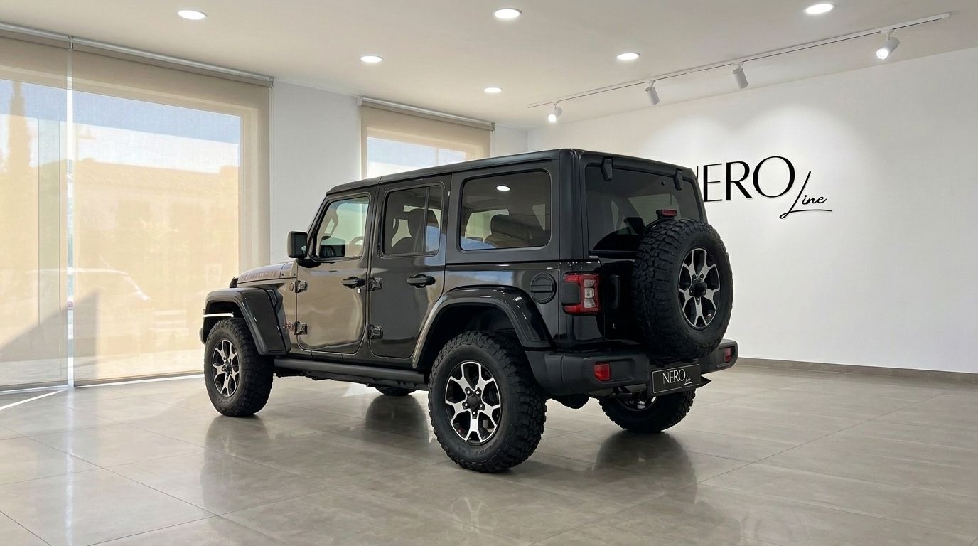 El Jeep Rubicon negro se exhibe desde un ángulo trasero tres cuartos en una luminosa y moderna sala de exposición en Ibiza.