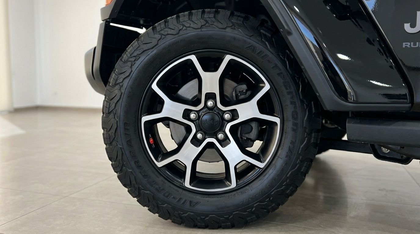 Primer plano del robusto neumático todoterreno y la llanta bicolor del Jeep Rubicon negro, mostrando su diseño en Ibiza.