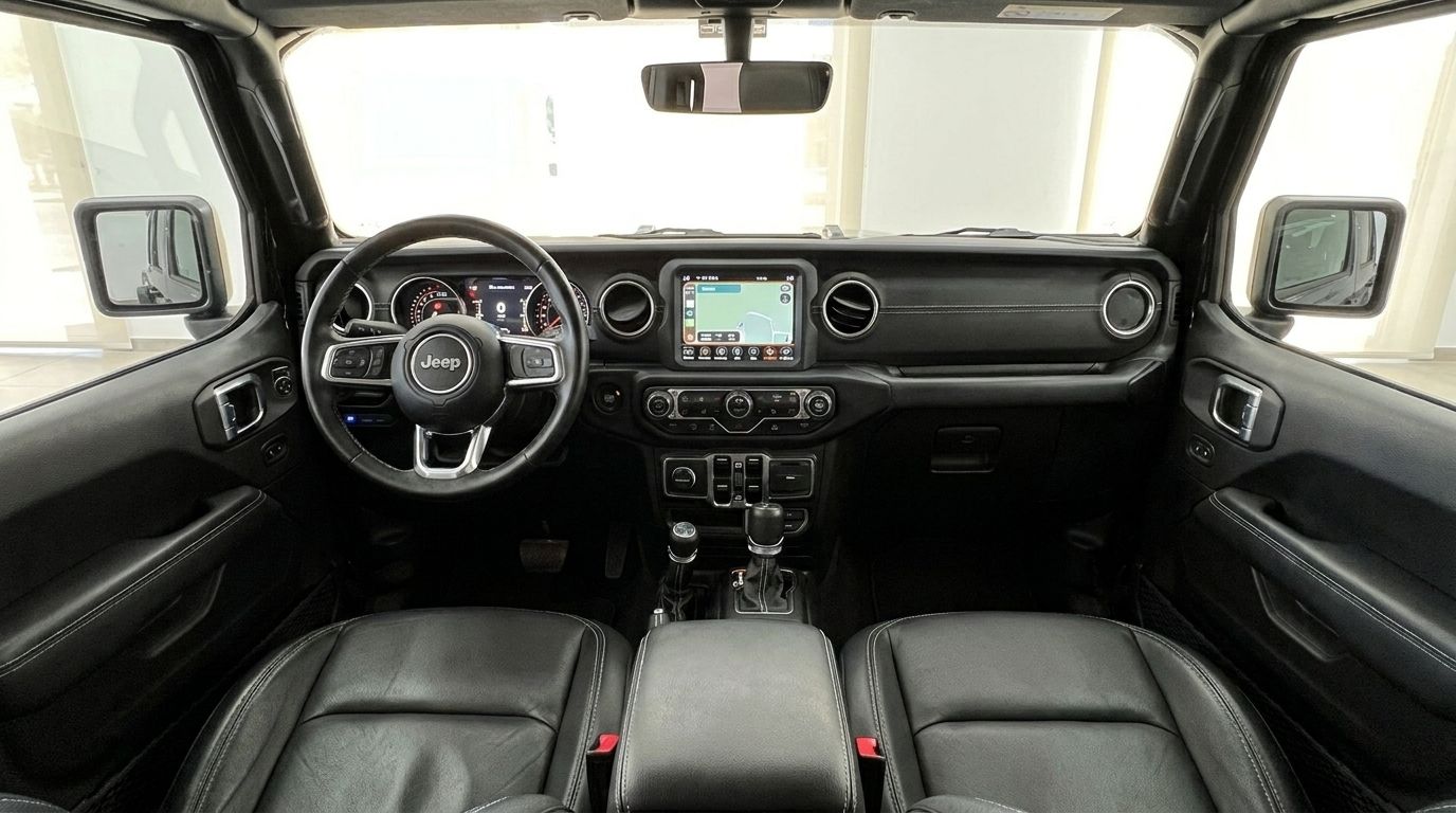 El interior del Jeep Rubicon en Ibiza, mostrando asientos de cuero negro, el volante y el salpicadero central con su pantalla de infoentretenimiento.
