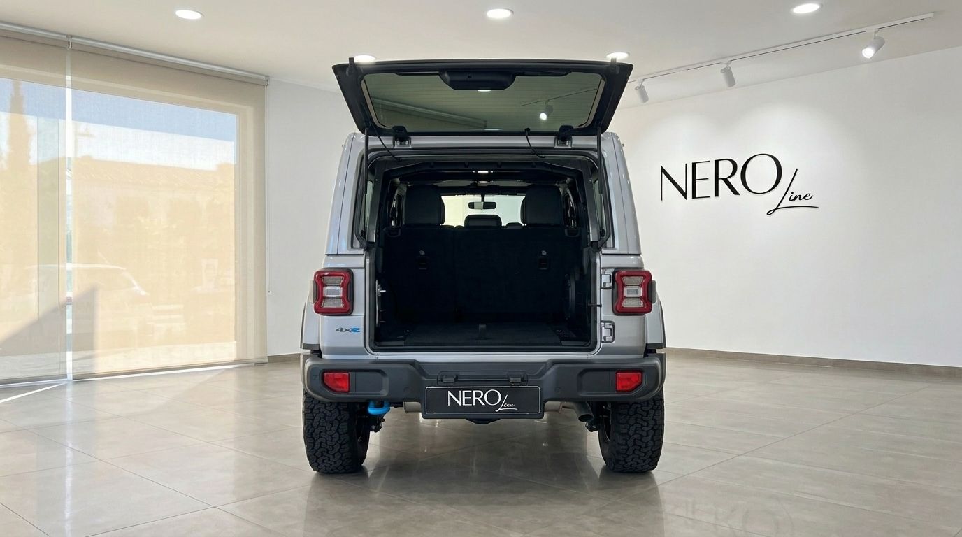 The rear view of a silver Jeep Rubicon 4xe Hybrid Cabrio with its boot open, parked in a showroom in Ibiza.