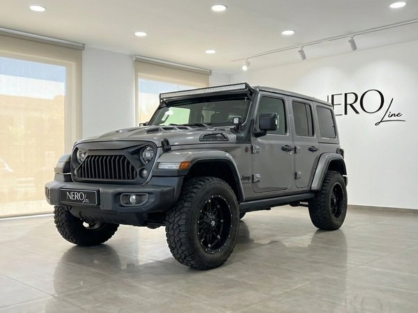 Jeep Sahara — Metallic grey exterior in Alicante The metallic grey Jeep Sahara, featuring a front three-quarter view of its rugged exterior, is showcased in a modern Alicante showroom.