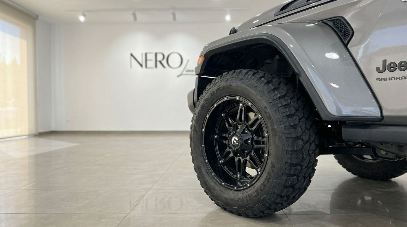 Close-up of the rugged front wheel and metallic grey fender of the Jeep Sahara, showcased in a modern Alicante showroom.