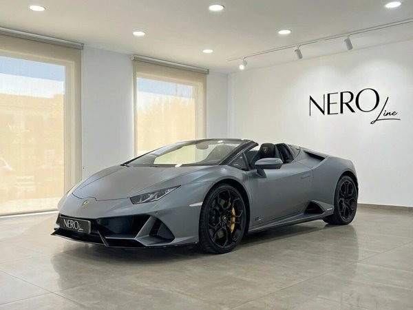 Lamborghini Huracan Evo Spyder — Showroom Ibiza La Lamborghini Huracan Evo Spyder gris mat est présentée de trois quarts avant dans un showroom lumineux à Ibiza.