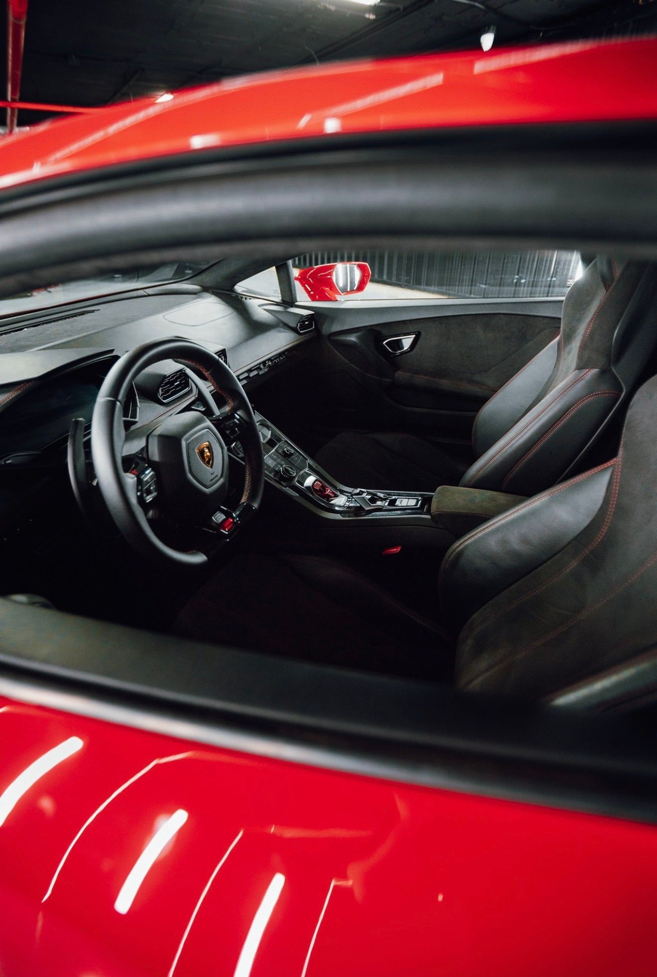 El lujoso interior del Lamborghini Huracan LP610-4 rojo en Madrid, mostrando el volante, el salpicadero y los asientos de cuero negro con costuras rojas.