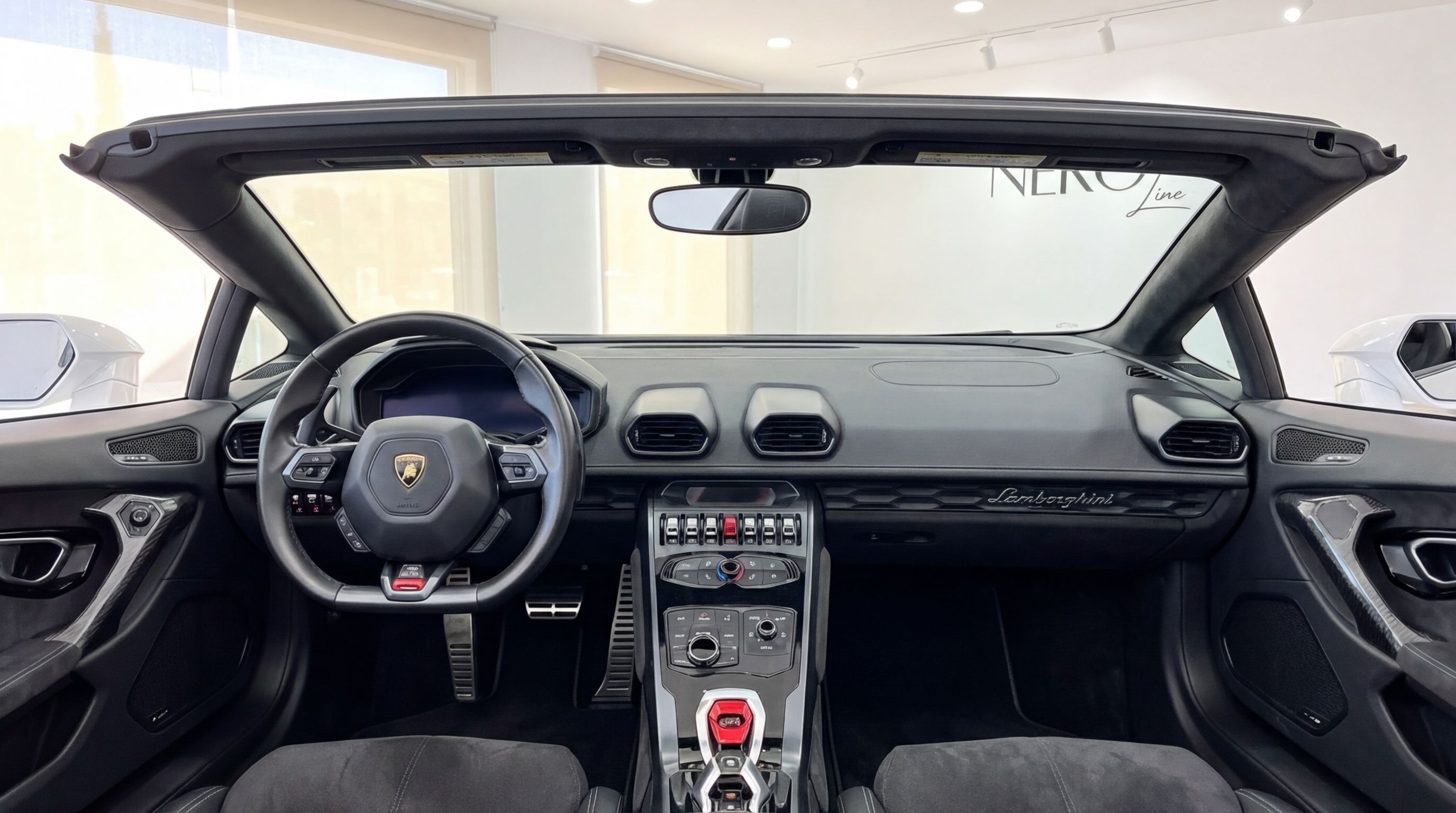 The luxurious black interior and dashboard of the Lamborghini Huracan Spyder convertible, showcasing the steering wheel and open roof.
